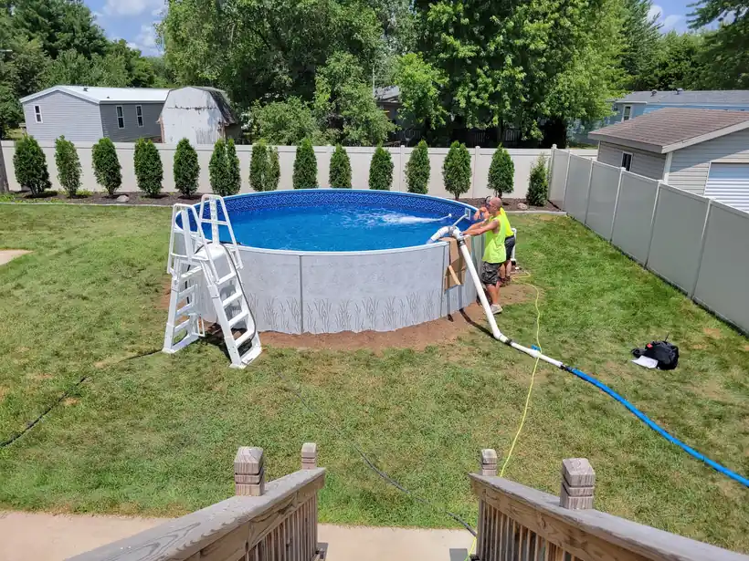 A crew member at the ladder of an above-ground pool as it fills from a hose