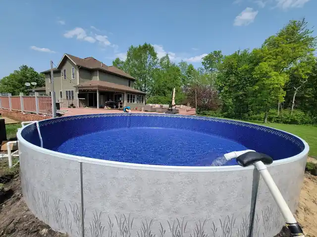 A round pool with grey walls and a house behind it