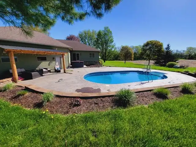 A freeform in-ground pool on a stamped patio with a covered pergola