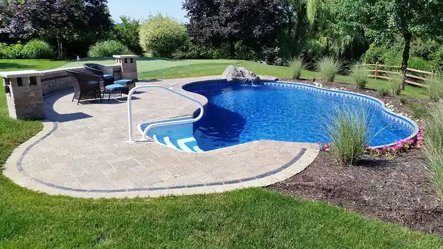 A kidney-shaped in-ground pool beside a paver patio and an outdoor kitchen