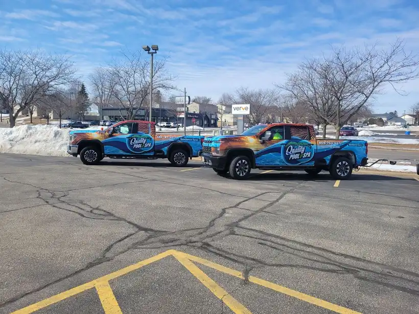 Two Quality Pool & Spa pickup trucks wrapped in the company's blue oval logo, parked side by side